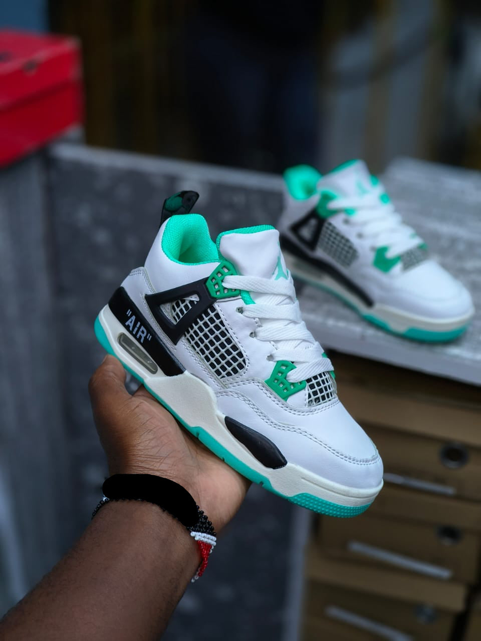 White sneakers with green accents held by a hand, with a blurred background