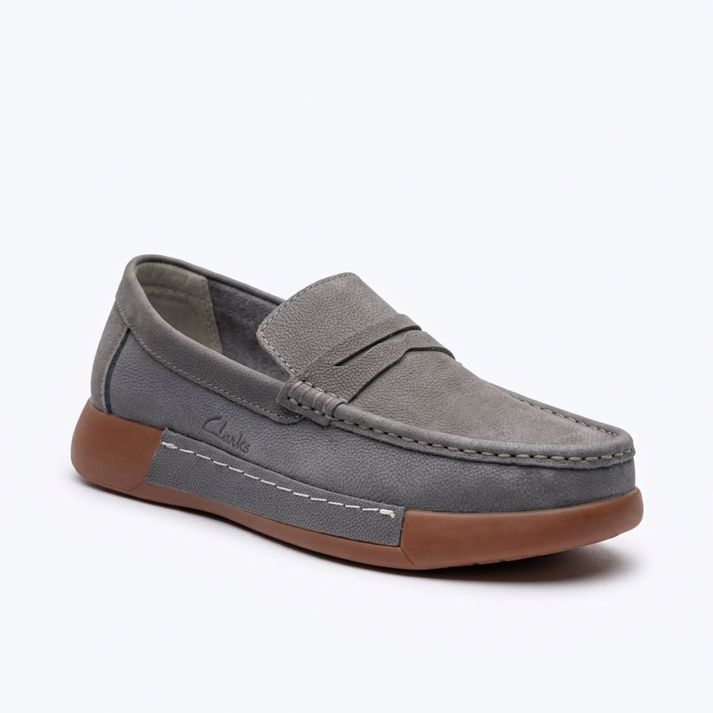 Grey slip-on loafer with front strap, moc-toe stitching and brown sole on white background