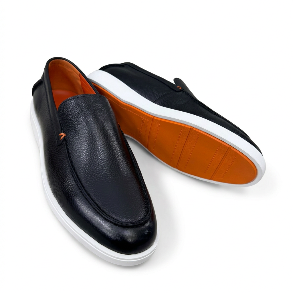 Black slip-on loafers showing orange outsole and white sole edge on white